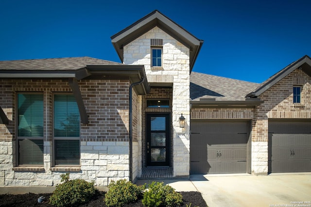 doorway to property with driveway, an attached garage, a shingled roof, stone siding, and brick siding