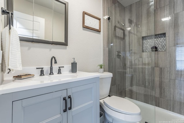 bathroom featuring vanity, toilet, a shower stall, and a textured wall