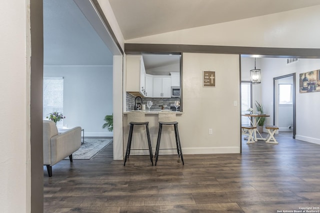 kitchen featuring decorative backsplash, vaulted ceiling, white cabinetry, stainless steel microwave, and a kitchen breakfast bar