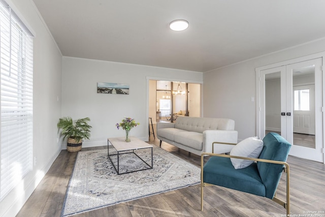 living area featuring a notable chandelier, ornamental molding, wood finished floors, french doors, and baseboards