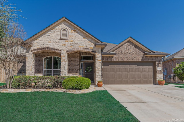 french country style house with a front yard, an attached garage, concrete driveway, and stone siding