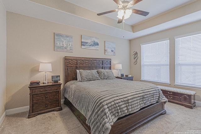 bedroom featuring light carpet, ceiling fan, baseboards, and a tray ceiling