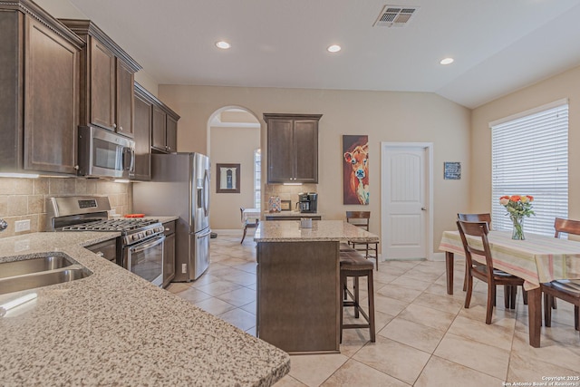 kitchen with arched walkways, dark brown cabinetry, a kitchen breakfast bar, and stainless steel appliances