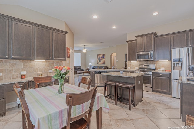 kitchen featuring backsplash, dark brown cabinets, light stone countertops, light tile patterned floors, and appliances with stainless steel finishes