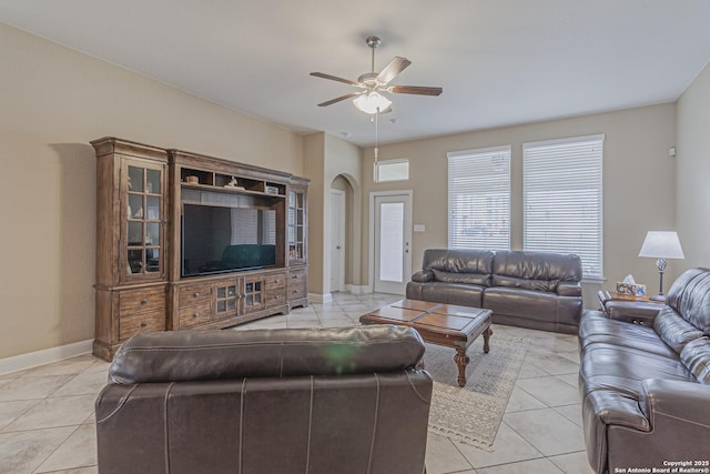 living room featuring light tile patterned floors, baseboards, arched walkways, and a ceiling fan