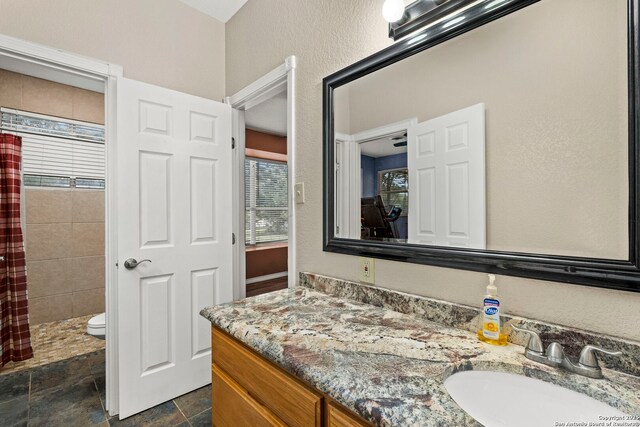 bathroom with toilet, stone finish floor, a shower with shower curtain, vanity, and a textured wall