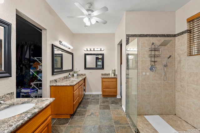 bathroom featuring ceiling fan, two vanities, a tile shower, stone finish floor, and a sink