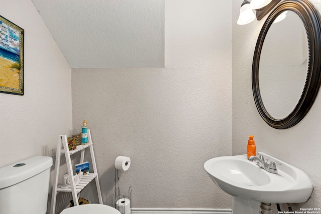 bathroom featuring a sink, lofted ceiling, toilet, and a textured wall