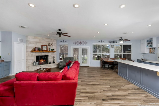 living room featuring visible vents, a fireplace, light wood-type flooring, and a ceiling fan