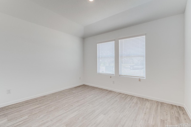 unfurnished room with baseboards, light wood-style floors, and vaulted ceiling