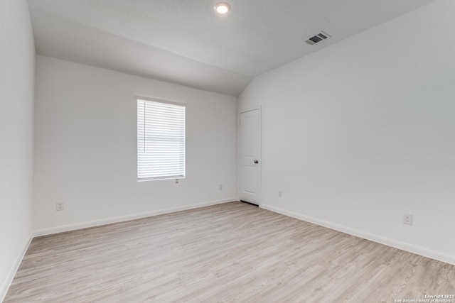 unfurnished room featuring visible vents, lofted ceiling, light wood-type flooring, and baseboards