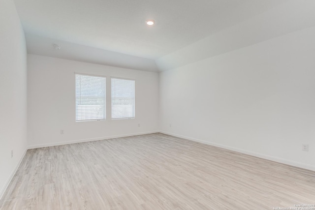 spare room with lofted ceiling, baseboards, and light wood-type flooring