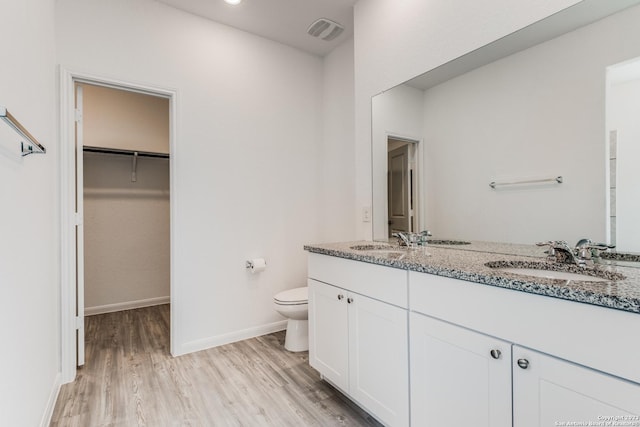 bathroom with visible vents, toilet, a sink, wood finished floors, and double vanity