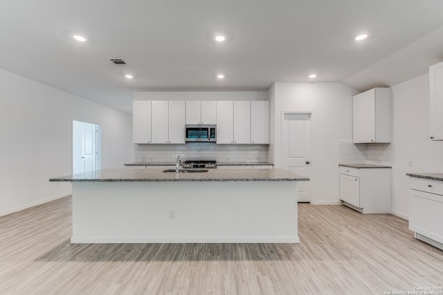 kitchen with stainless steel microwave, light wood finished floors, and dark stone counters