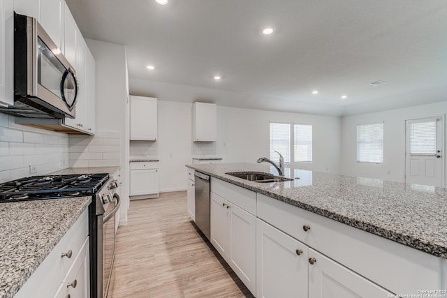 kitchen featuring a sink, light wood-type flooring, light stone counters, and appliances with stainless steel finishes