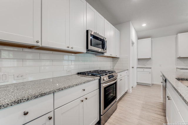 kitchen with light wood-type flooring, tasteful backsplash, white cabinetry, stainless steel appliances, and light stone countertops