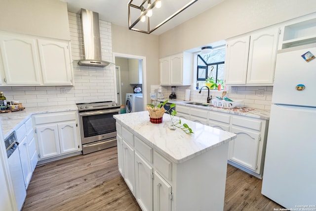 kitchen featuring wall chimney range hood, dishwashing machine, stainless steel range with electric stovetop, freestanding refrigerator, and independent washer and dryer