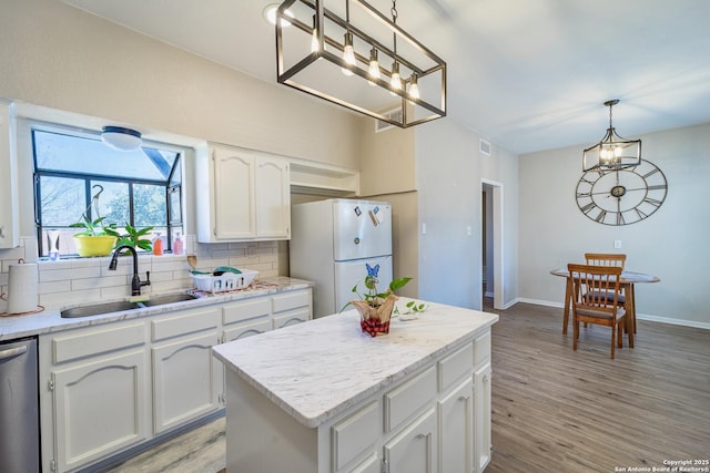 kitchen featuring a sink, backsplash, freestanding refrigerator, a notable chandelier, and stainless steel dishwasher