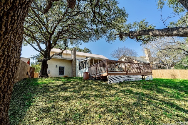 back of house with stucco siding, a lawn, a deck, and fence