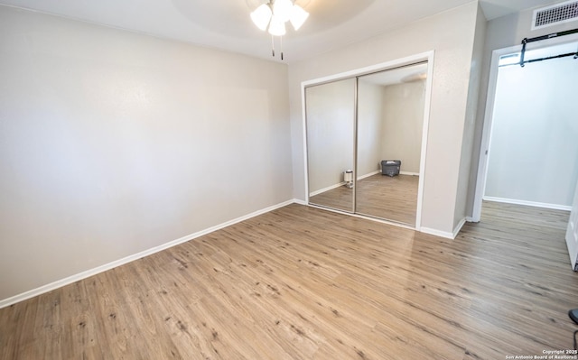 unfurnished bedroom featuring wood finished floors, visible vents, a closet, and baseboards