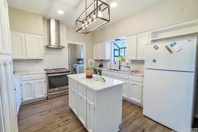 kitchen featuring stainless steel electric stove, freestanding refrigerator, an inviting chandelier, wall chimney range hood, and washing machine and clothes dryer