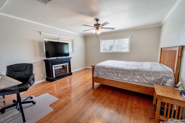 bedroom featuring a glass covered fireplace, crown molding, baseboards, and wood-type flooring