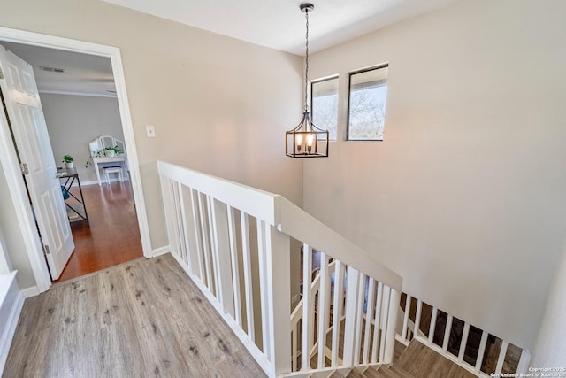 hallway featuring wood finished floors, visible vents, baseboards, an upstairs landing, and a chandelier