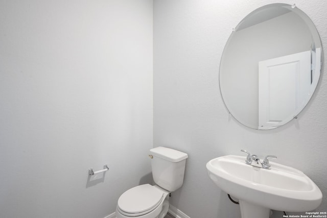 half bathroom with a sink, baseboards, and toilet