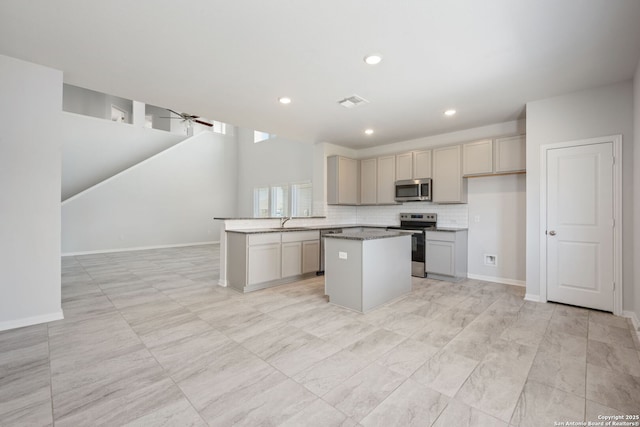 kitchen with a kitchen island, a sink, open floor plan, appliances with stainless steel finishes, and tasteful backsplash