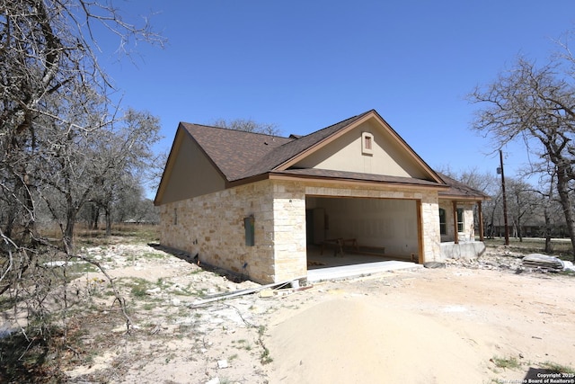 view of property exterior with an attached garage, a shingled roof, stucco siding, stone siding, and dirt driveway