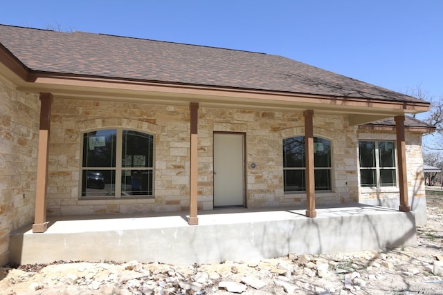 view of exterior entry featuring covered porch, stone siding, and a shingled roof