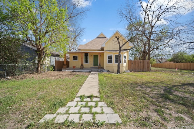 bungalow with roof with shingles, covered porch, a front yard, and fence