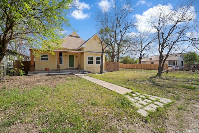 bungalow-style home featuring covered porch, a shingled roof, a front yard, and fence