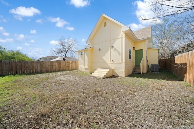 rear view of property featuring entry steps, a fenced backyard, central AC, and a shingled roof