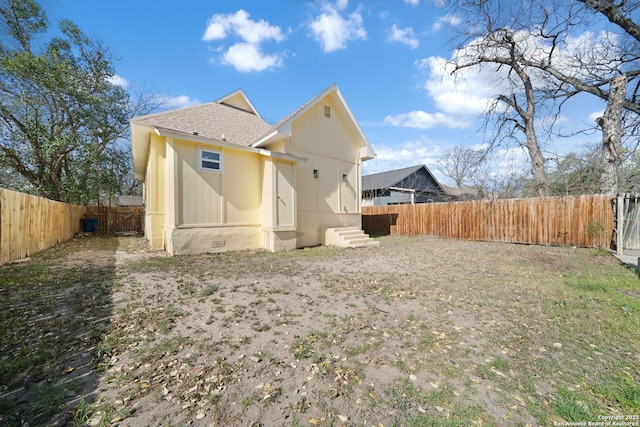 back of property with entry steps, a fenced backyard, and roof with shingles