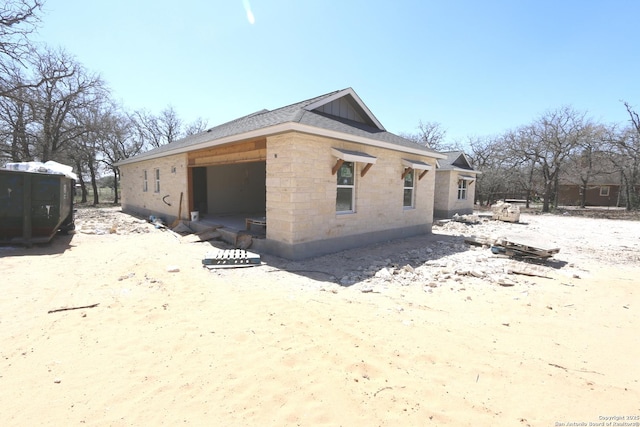 view of property exterior featuring stone siding and roof with shingles