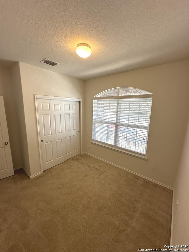 unfurnished bedroom featuring visible vents, baseboards, carpet, a closet, and a textured ceiling