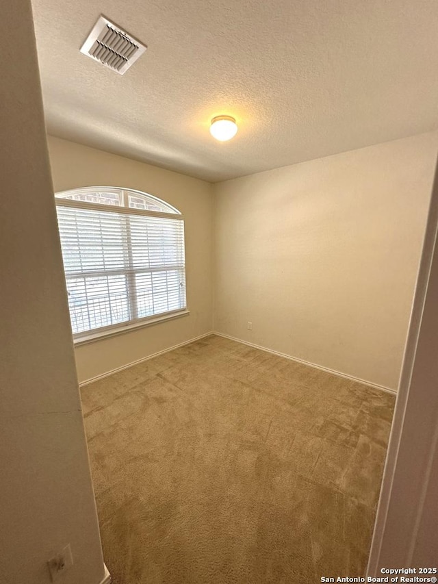 carpeted empty room with visible vents, a textured ceiling, and baseboards