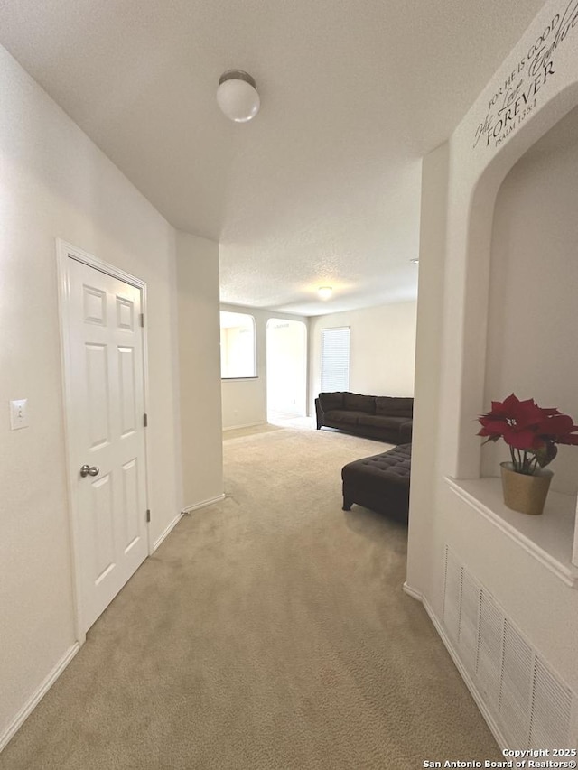 corridor with visible vents, arched walkways, baseboards, and carpet floors