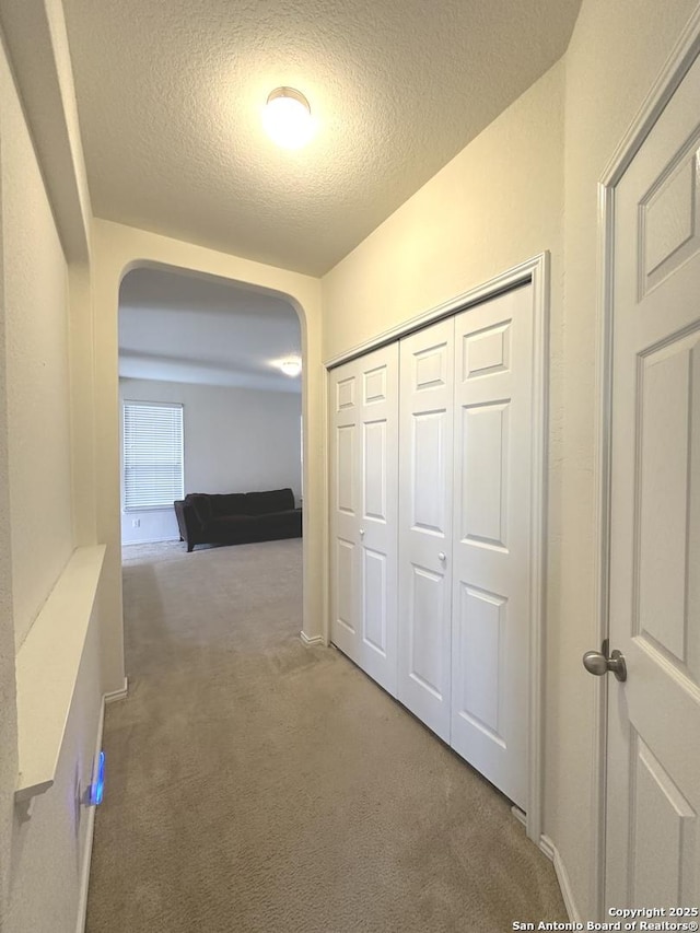 corridor featuring arched walkways, a textured ceiling, and carpet