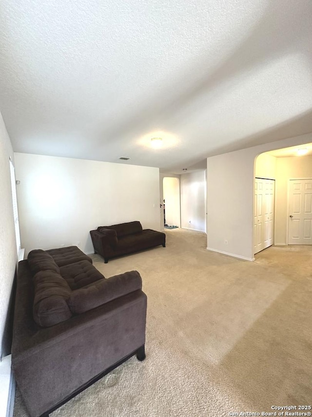 living area with visible vents, arched walkways, light colored carpet, and a textured ceiling