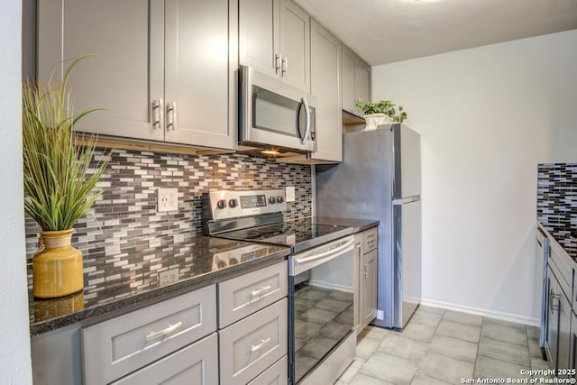 kitchen with tasteful backsplash, baseboards, dark stone countertops, appliances with stainless steel finishes, and light tile patterned flooring