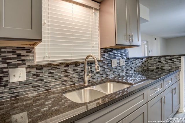 kitchen featuring a sink, decorative backsplash, gray cabinets, and dark stone countertops