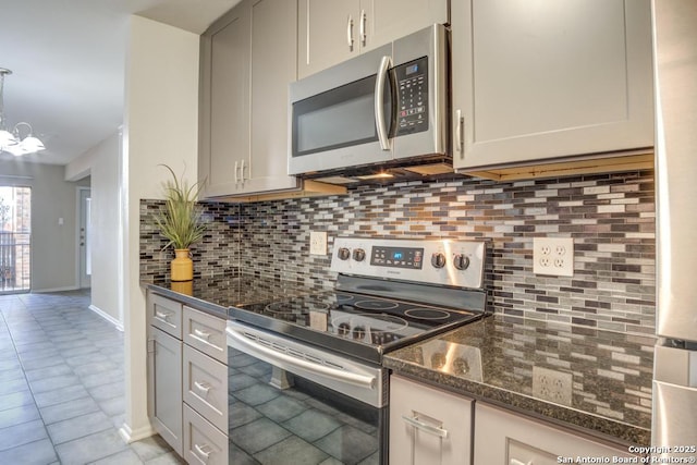 kitchen featuring dark stone countertops, tasteful backsplash, an inviting chandelier, appliances with stainless steel finishes, and light tile patterned floors