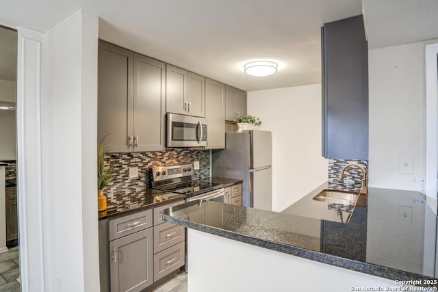 kitchen with tasteful backsplash, gray cabinetry, appliances with stainless steel finishes, a peninsula, and a sink