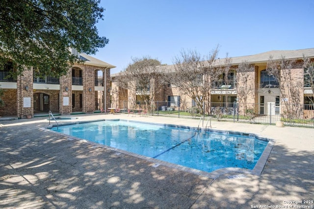 pool with a patio, a community hot tub, and fence