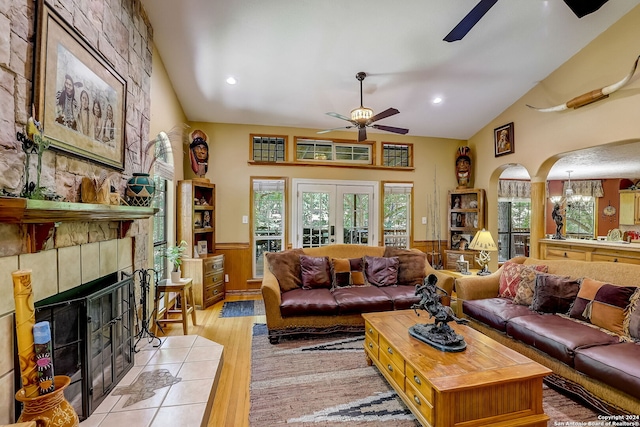 living area with a wainscoted wall, a tiled fireplace, arched walkways, light wood-style floors, and ceiling fan