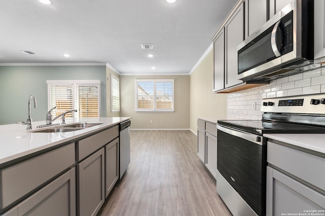 kitchen featuring crown molding, decorative backsplash, gray cabinets, stainless steel appliances, and a sink