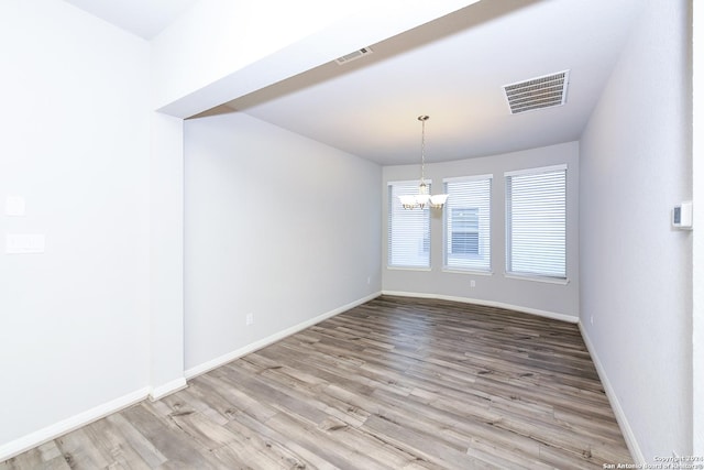 unfurnished dining area featuring a notable chandelier, wood finished floors, visible vents, and baseboards