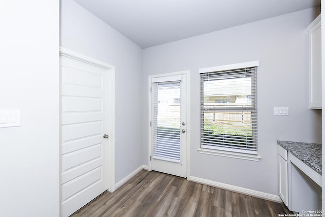 doorway with baseboards and dark wood-type flooring